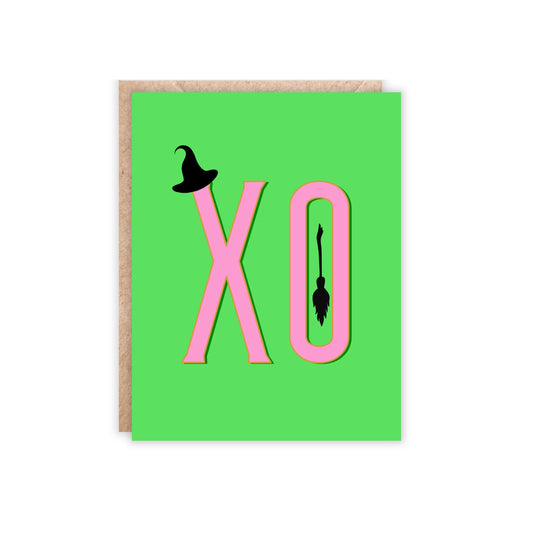 Green card with xo in pink and has a small witch hat and broomstick