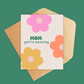 A2 size greeting card. Front of Card has pink, orange and yellow large daisies, with text reading Mom, you're amazing. Includes kraft envelope. Inside of card is blank. 
