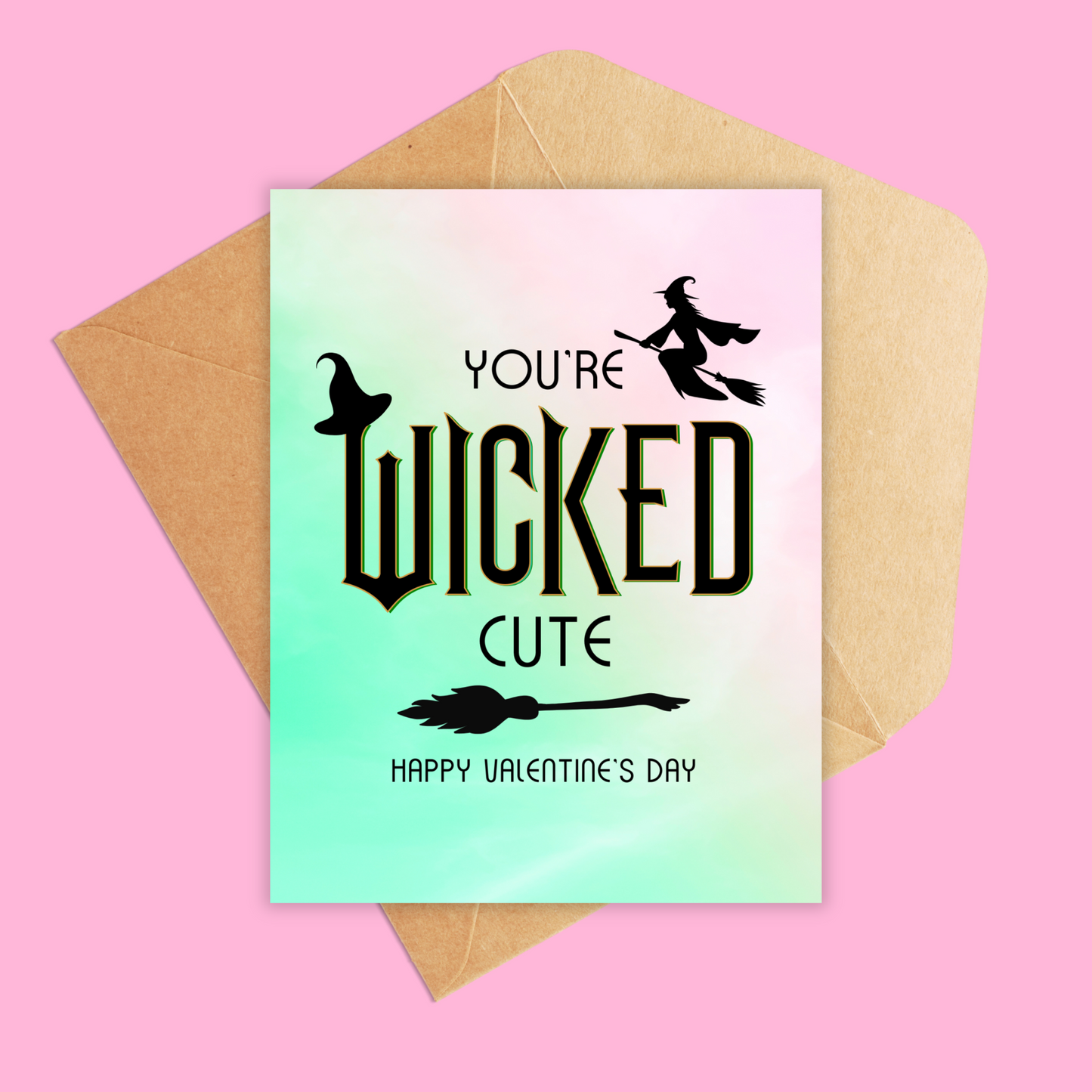 Greeting card shown with brown kraft envelop. Pink and green ombre colored background with the text You're wicked cute happy valentine's day. Has a witch hat, broomstick and flying witch on the card