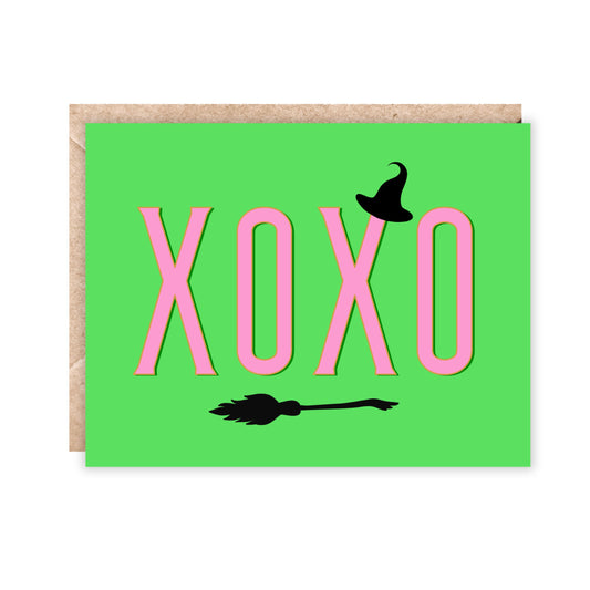 Landscape greeting card with a bright green background and xoxo going across in pink. Has a small witch hat and broomstick in black. 